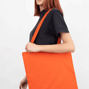 Woman with red hair carrying an orange cotton canvas tote bag.